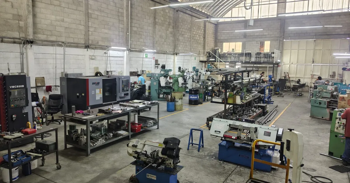Nave del taller con centro de maquinado CNC, fresadoras, tornos y racks de barras de acero bajo techo de lámina