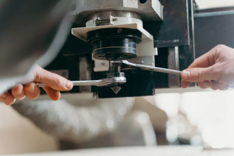 Manos ajustando con llaves el cabezal de una máquina CNC